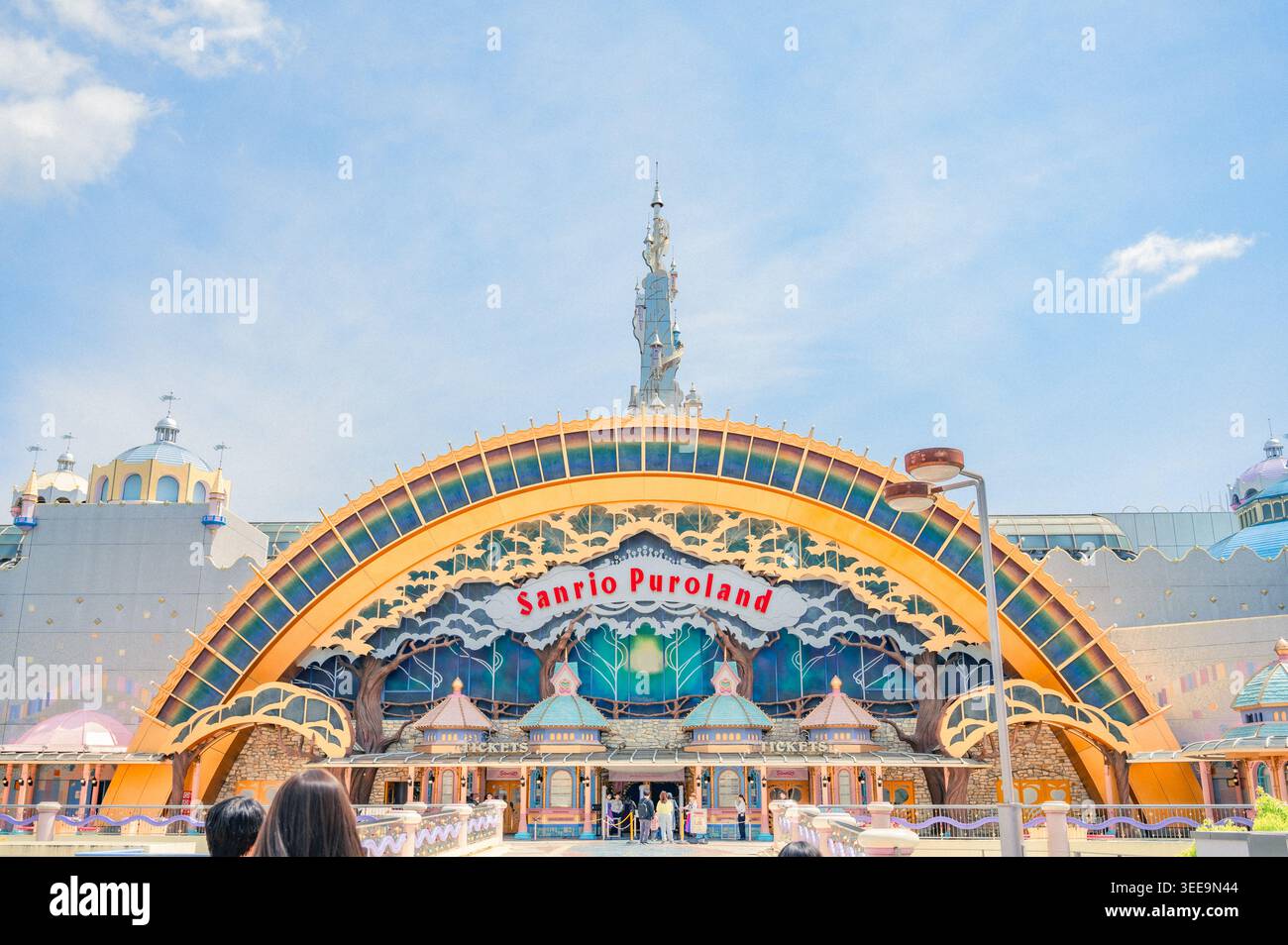 Eintritt zum Sanrio Puroland in Tokio mit farbenfrohem Regenbogenbogen, dekorativen Türmen und Besuchern, die sich dem Ticketbereich nähern. Stockfoto