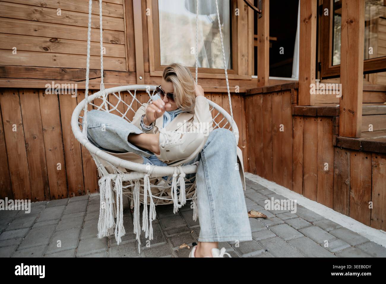 Frau, die sich in einem Hängestuhl auf einer hölzernen Veranda entspannt Stockfoto