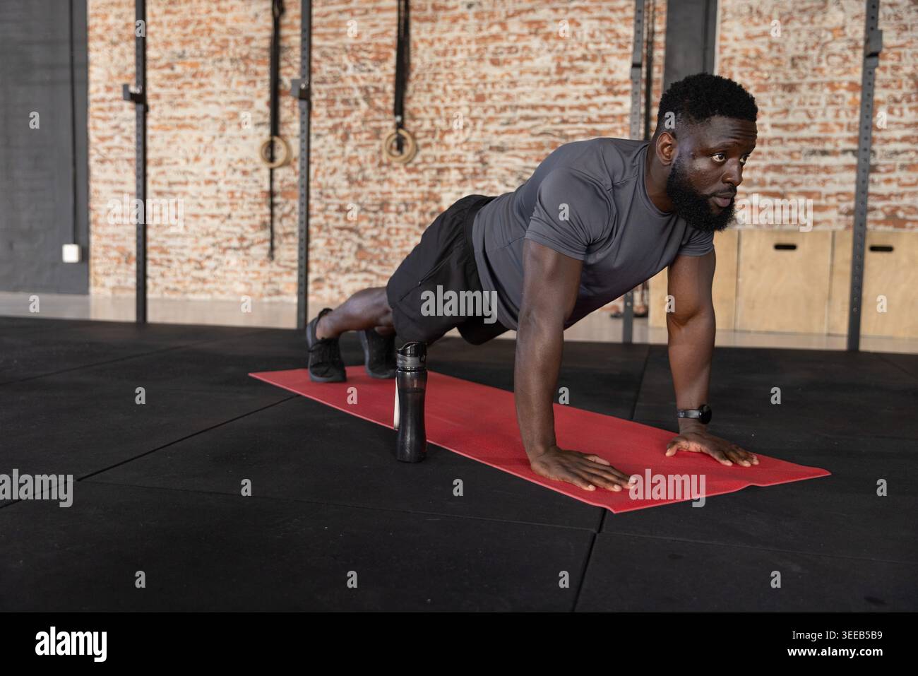 Auf roter Matte im Fitnessstudio, Afroamerikaner in grauem Hemd, Wasserflasche in der Nähe Stockfoto