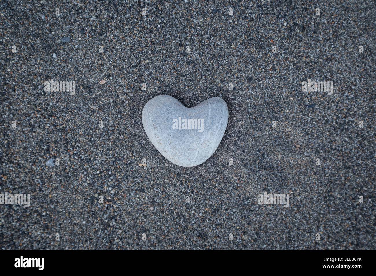 Glatter, herzförmiger Stein auf körnigem Sand - ein natürliches Symbol der Liebe. Perfekt für Valentinstag-Themen, Wellness-Branding oder Umweltkonzepte Stockfoto