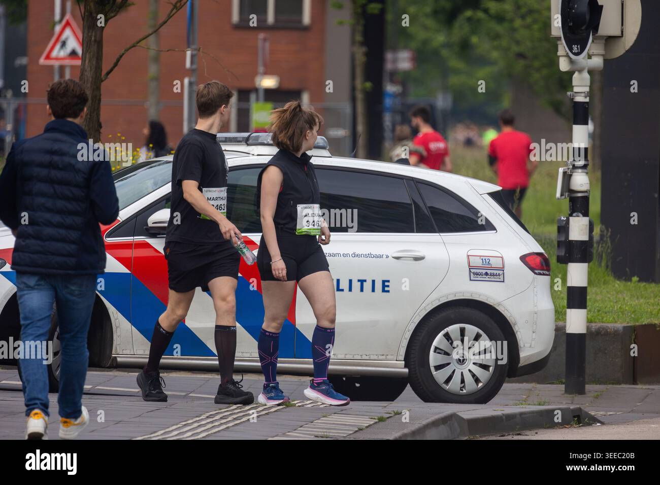 Utrecht, Region Utrecht, Niederlande - 09.06.2025: Läufer, die während des Utrecht Science Park Marathon an einem niederländischen Polizeiauto vorbeifahren. Ehrliche urbane Szene von Stockfoto
