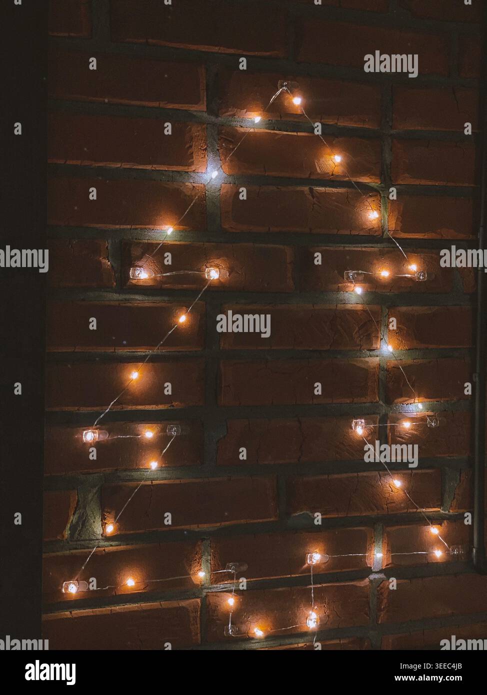 Warme Feenlichter leuchten auf rustikalen Ziegelwänden in gemütlicher Einrichtung - Smartphone-aufgenommenes Stockfoto