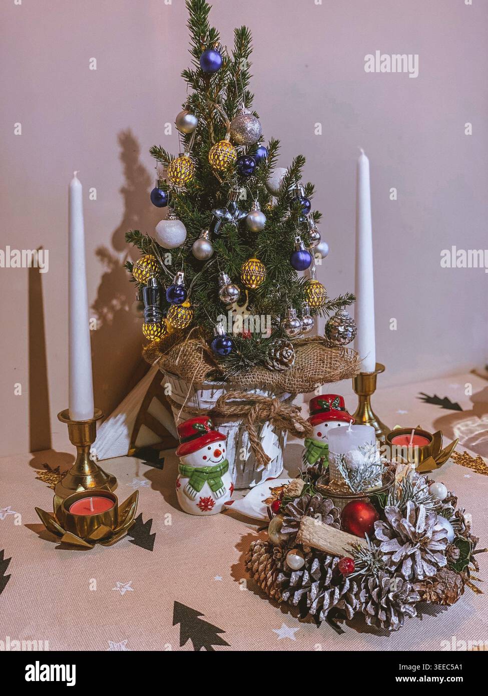 Geschmückter Weihnachtsbaum mit Kerzen auf dem Tisch, gemütliches festliches Festtagskomposition im Innenbereich - Smartphone-aufgenommenes Stockfoto