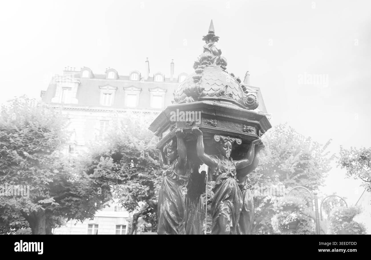 Typischer Pariser Trinkbrunnen mit gusseiserner Frauengruppe auf dem Stadtplatz. Retro-Foto im Alter. Schwarz-weiß. Stockfoto