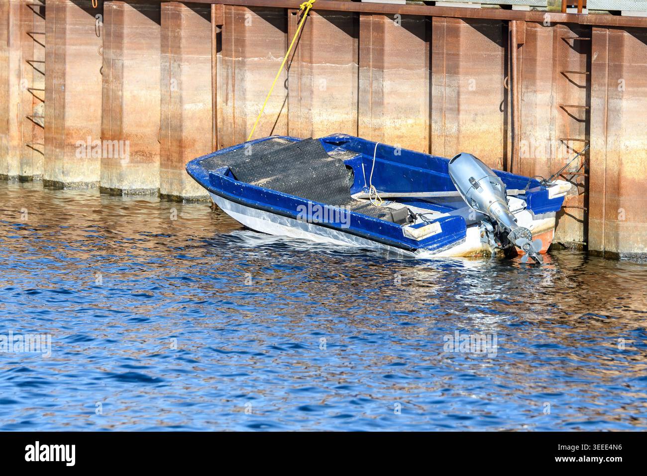 Ein kleines blaues Motorboot, gefesselt an einem Betonsteg. Ein Außenbordmotor befindet sich auf der Rückseite, wobei die Stütze aus dem Wasser herausgehoben ist. Eine Leiter am Heck le Stockfoto