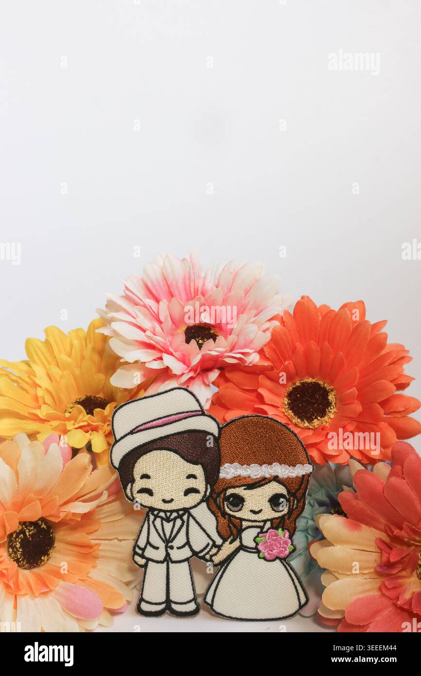 Niedliche Braut- und Bräutigam-Puppe mit bunten Gerbera-Blumen, die einen fröhlichen romantischen Hintergrund für die Hochzeit schaffen. Stockfoto