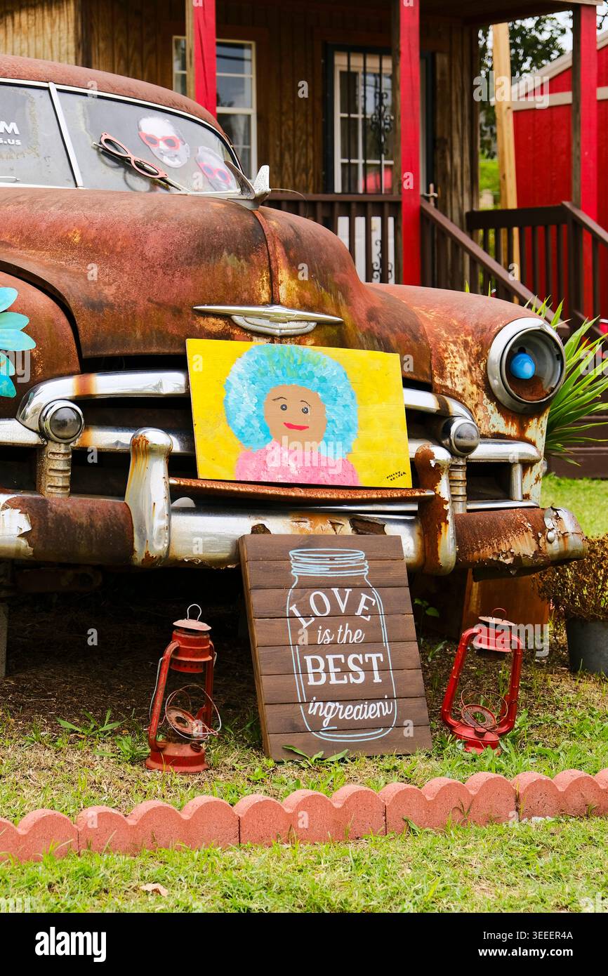 Liebe ist das beste Zutatenschild, das vor einem rostenden Oldtimer angebracht wird, als Hofkunst, die Frieden, Liebe und Mitgefühl in Montgomery Alabama, USA, fördert. Stockfoto