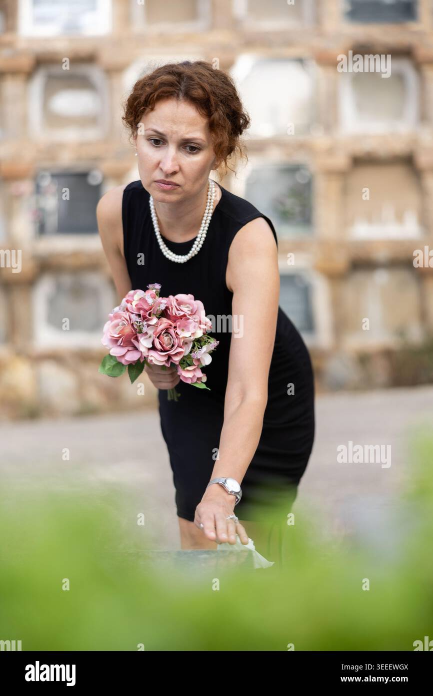 Eine Frau in schwarzem Kleid kam auf den Friedhof, um Blumen auf das Grab zu legen Stockfoto