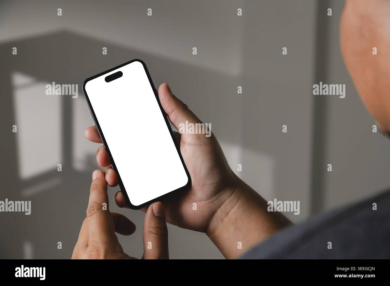 Nahaufnahme der Hände, die rahmenloses Smartphone mit leerem weißen Bildschirm unter weichem Innenlicht halten, geeignet für Mockup für mobile Apps, digitale Kommunikation, Stockfoto