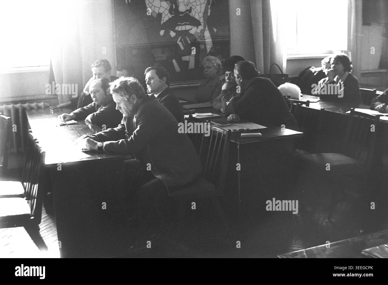 Slaviansk, 1983. Konferenzsaal der Armature-Isolator Factory (AIZ). Eine Seitenansicht des Publikums, die Männer und Frauen zeigt, die auf Holztischen sitzen und während einer Fabrikveranstaltung aufmerksam zuhören. Dieses Vintage-Schwarz-weiß-Foto fängt die authentische Atmosphäre der Epoche ein und spiegelt die täglichen Aktivitäten und Industriekultur der Region während der Sowjetzeit wider. Es dient als wertvolles historisches Dokument der lokalen Gemeinde, das das visuelle Gedächtnis der Menschen und ihres täglichen Lebens bewahrt und einen friedlichen Donbass zeigt. Stockfoto