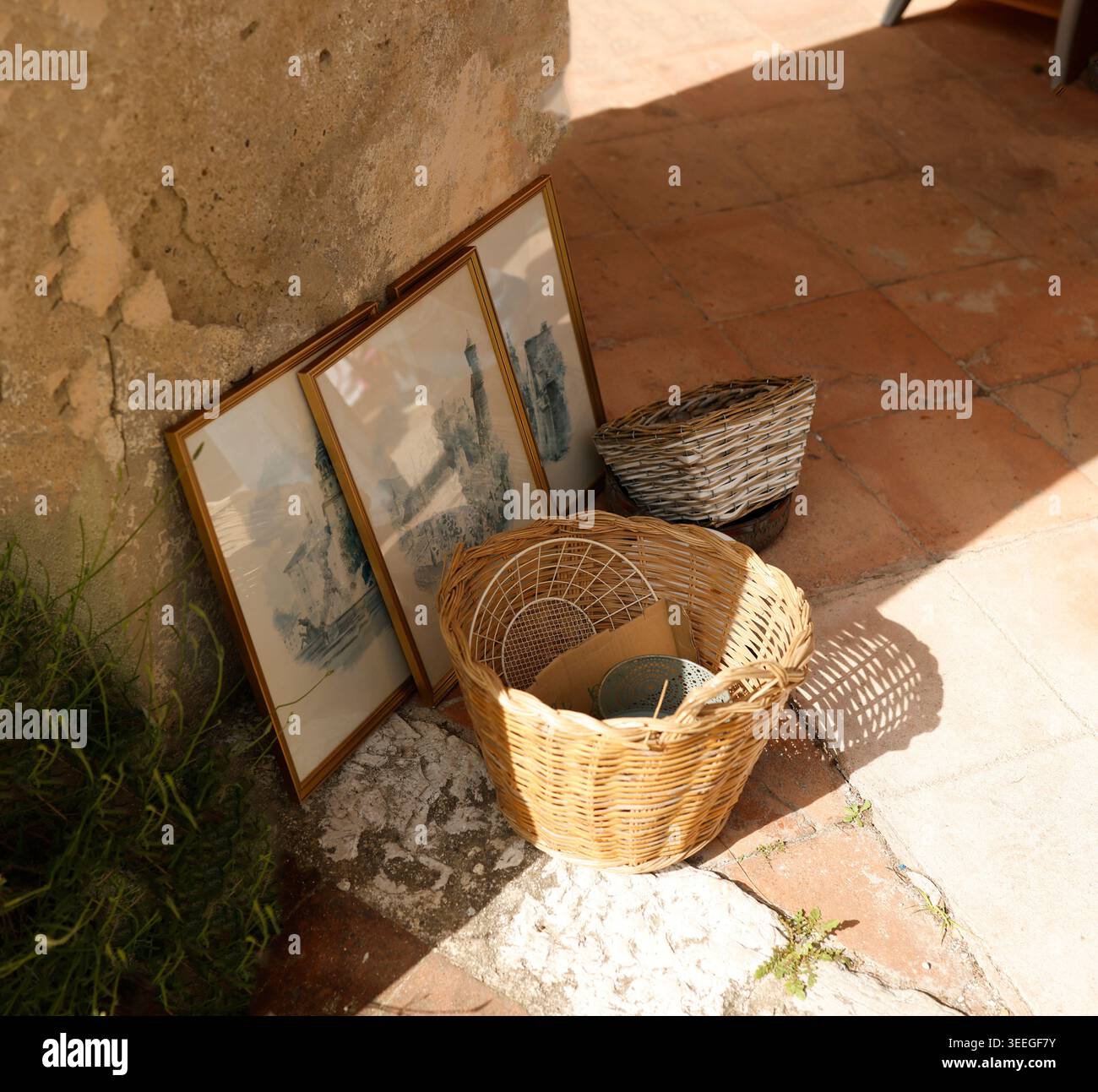 Antiker französischer Flohmarkt mit Vintage-Korbkörben und gerahmter Kunst von einer sonnendurchfluteten Steinmauer. Rustikale Außenpräsentation mit authentischem mediterranem Ambiente Stockfoto