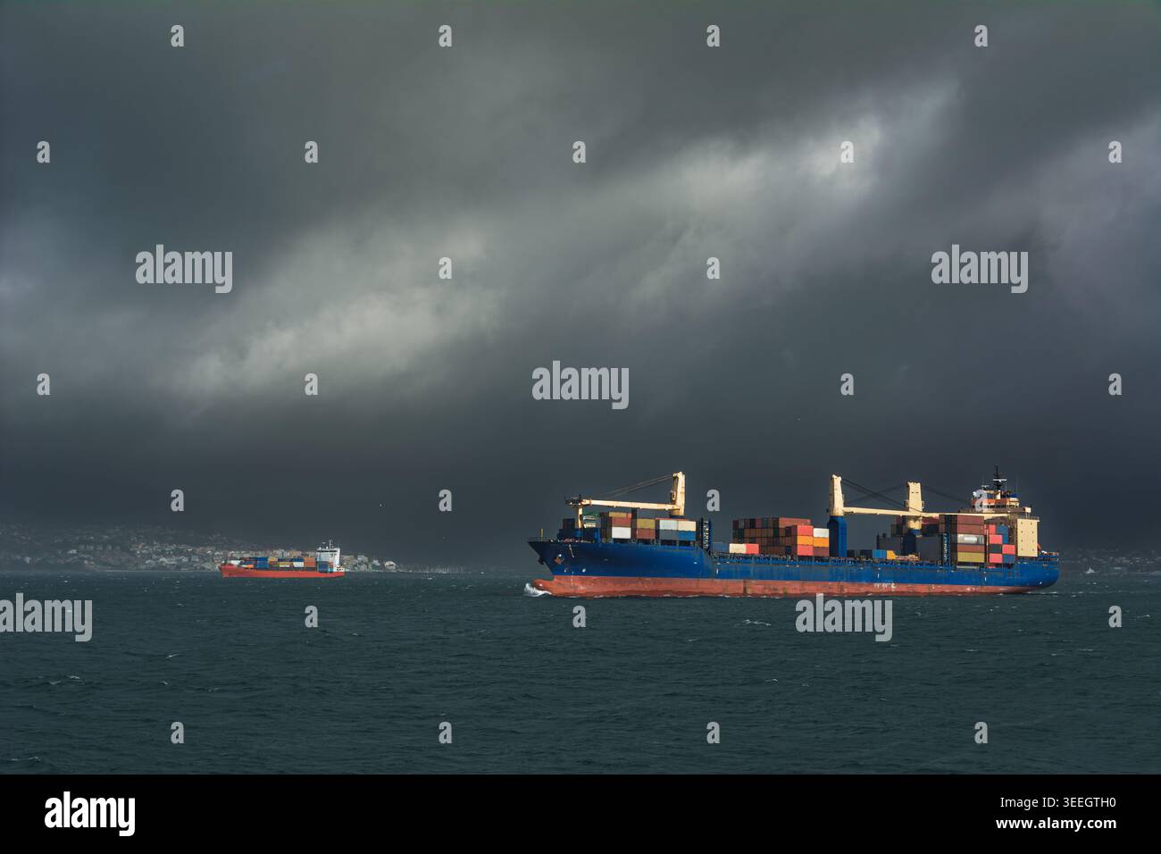 Zwei Containerschiffe, die raue Meere unter dramatischem stürmischem Himmel fahren, maritime Logistik Stockfoto