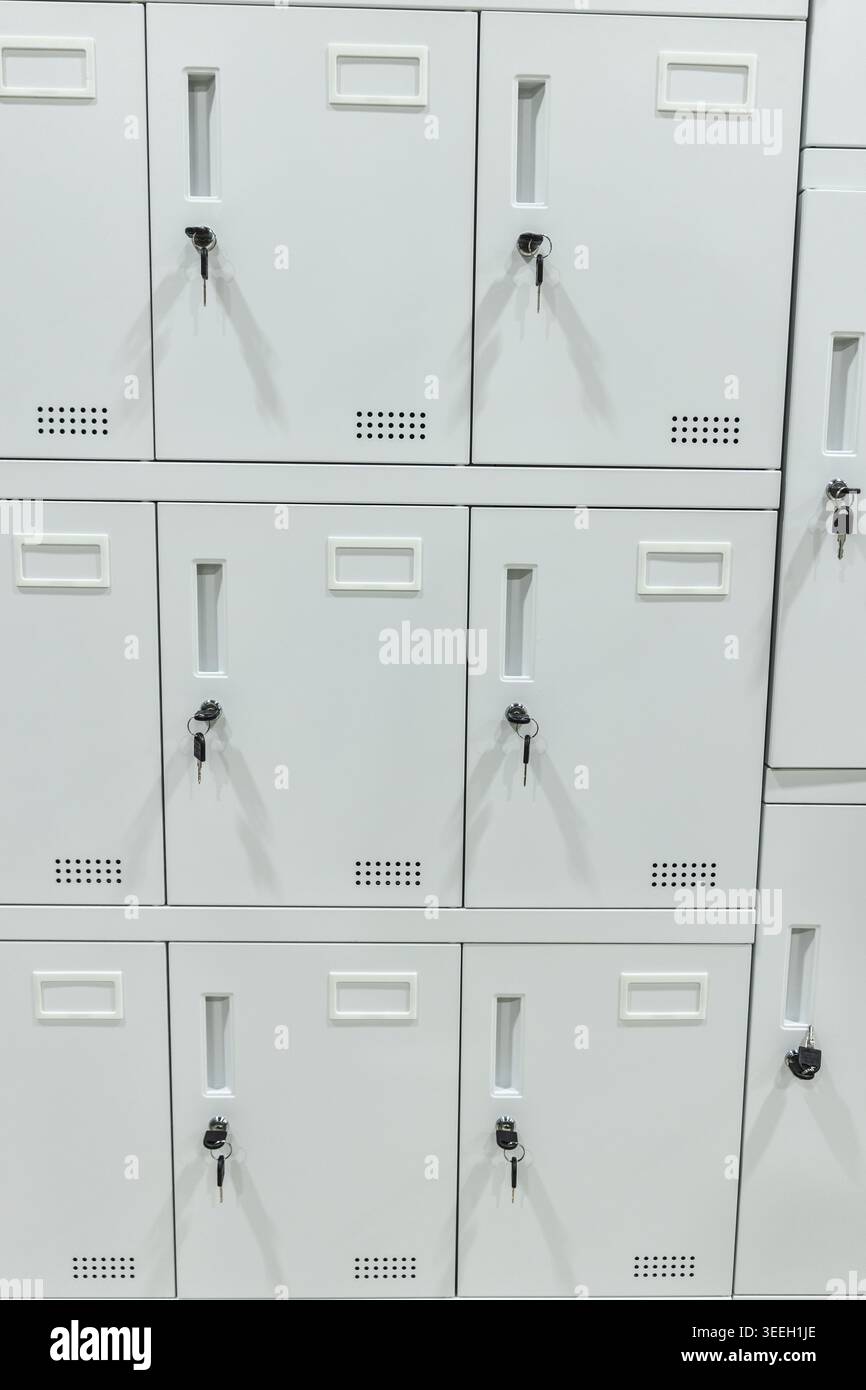 Weiße Schließfachschränke mit Schlüsseln, die sicher an der Wand angeordnet sind Stockfoto