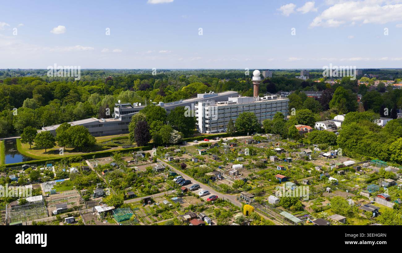 Blick aus der Vogelperspektive auf den KNMI Gebäudekomplex und Radarturm, umgeben von üppigen grünen Bäumen und gemeinschaftlichen Kleingärten in de Bilt, Utrecht, Niederlande Stockfoto