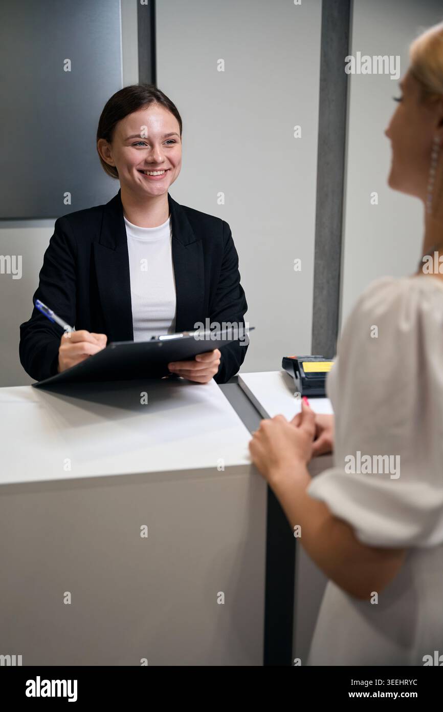 Glückliche kaukasische Frau, die am Service-Desk auf die Zwischenablage schreibt Stockfoto