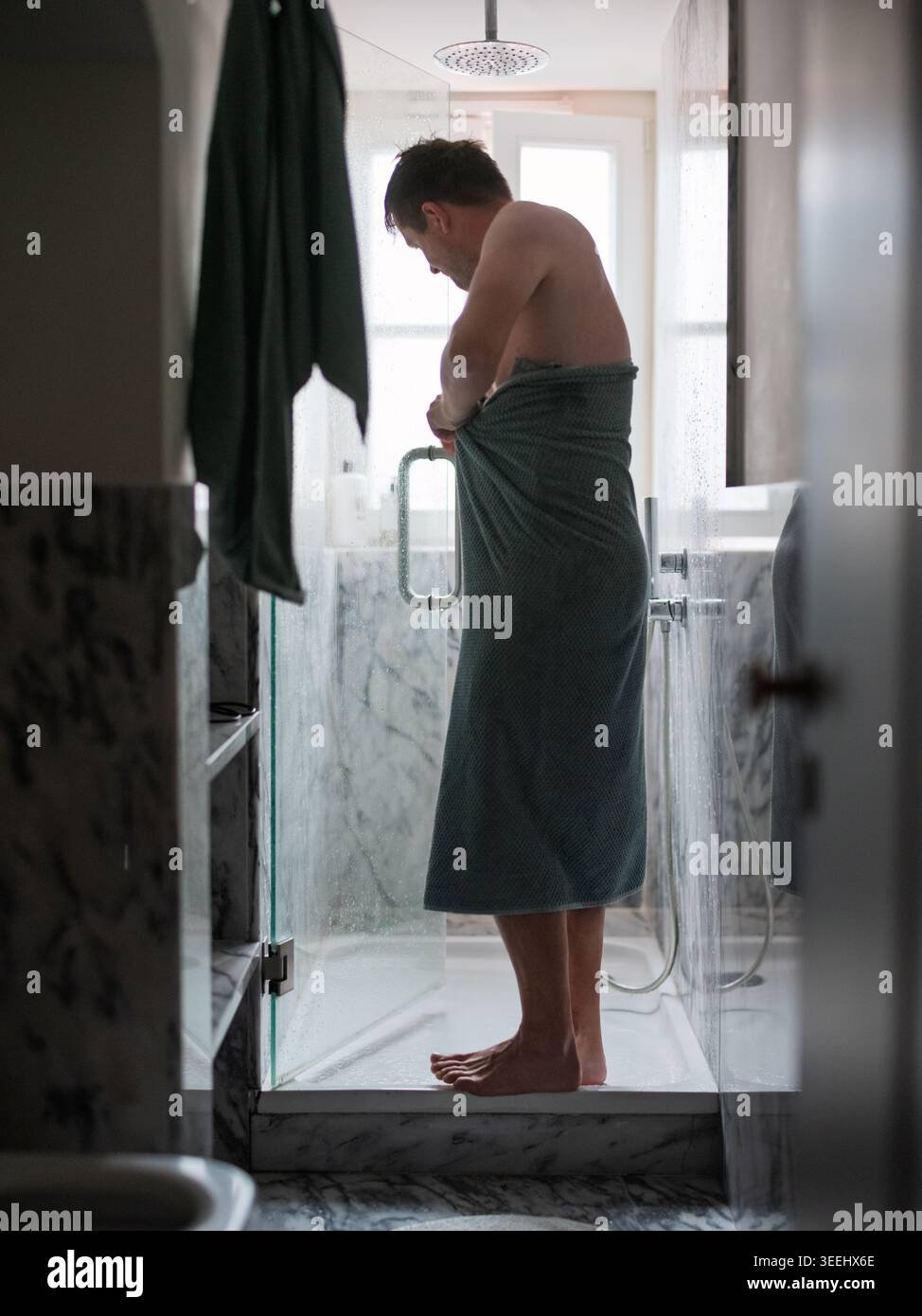 Ein erwachsener Mann hüllt sich in ein Handtuch, nachdem er in einem Marmorbad geduscht hat Stockfoto