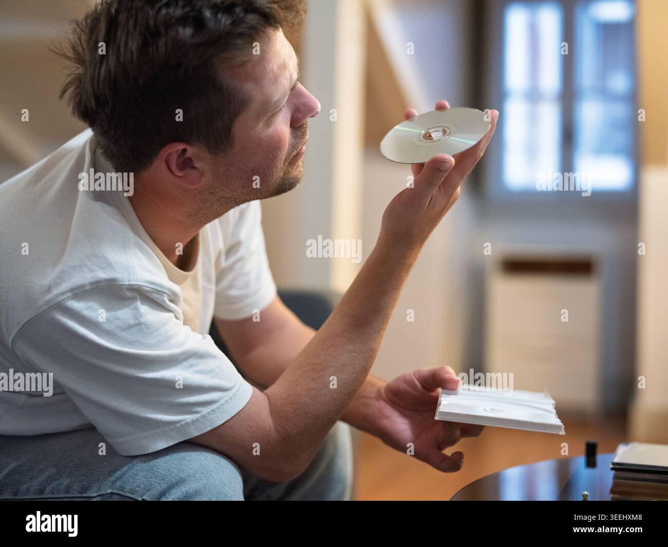 Mann, der sich eine CD anschaut, während er im Wohnzimmer sitzt Stockfoto
