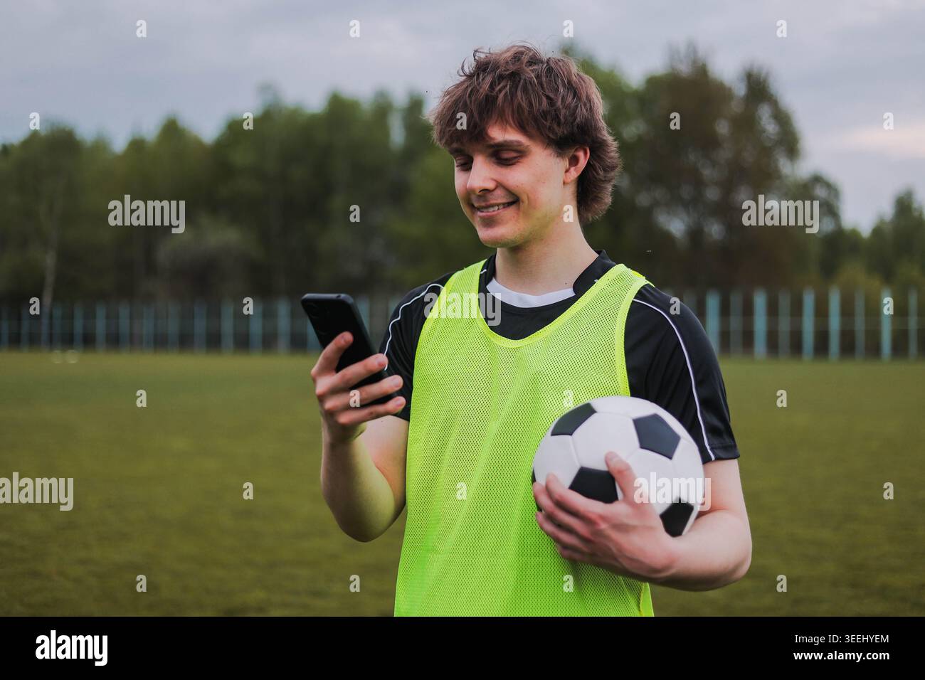 Hübsche junge Tennisspielerin, die während der Trainingspause mit dem Smartphone auf dem Platz steht. Stockfoto