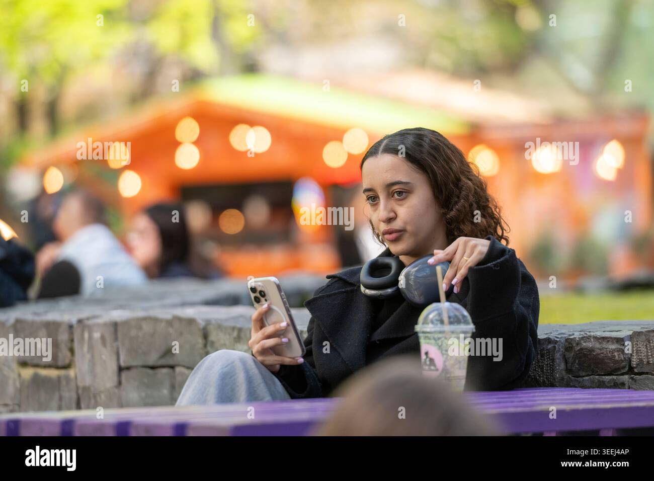 Junge Frau, die ein Smartphone benutzt, während sie sich draußen in Canary Wharf, London, entspannt. Stockfoto