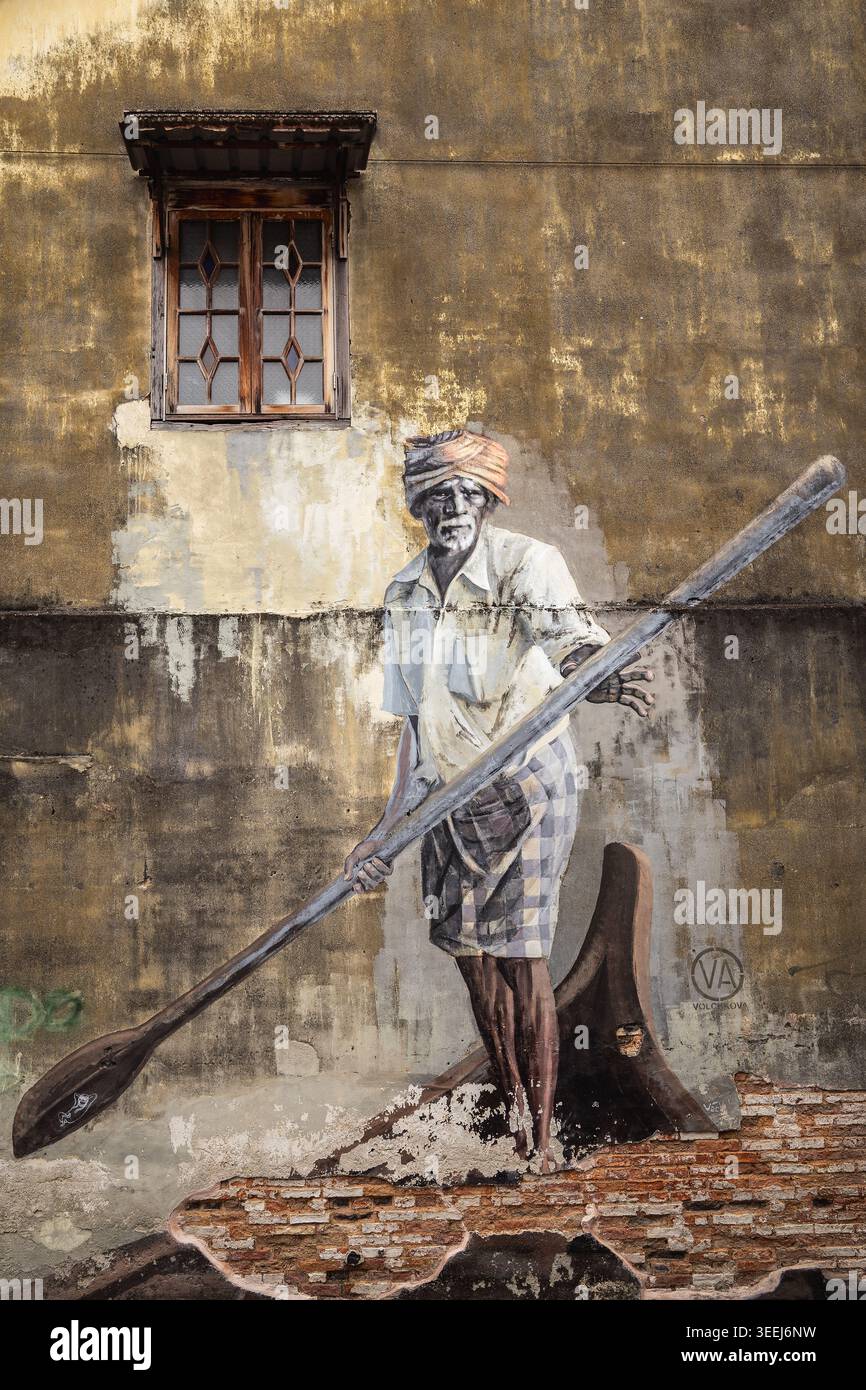 Das Wandgemälde des Indian Boatman in Penang, Malaysia, zeigt eine bemalte Figur, die ein Holzboot über eine strukturierte Wandfläche rudert. Stockfoto