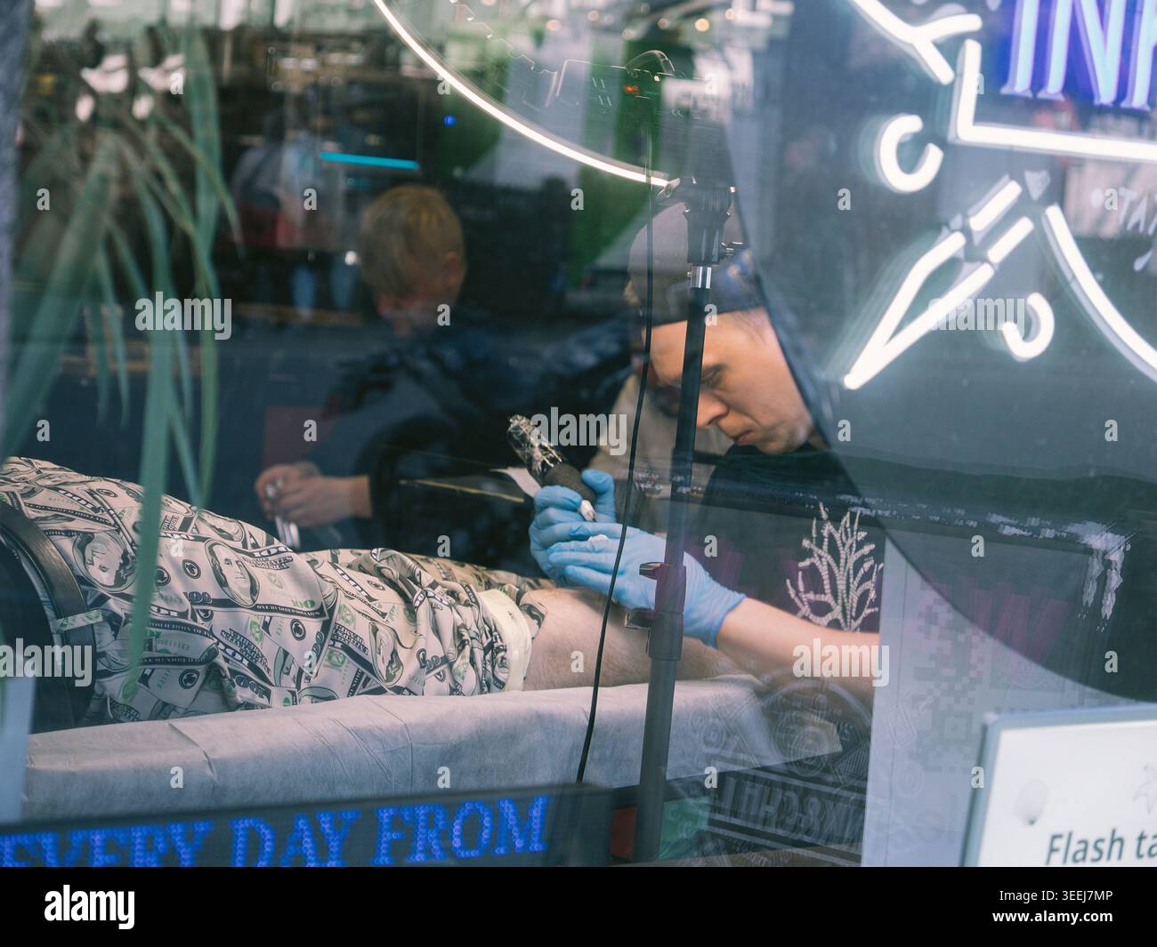 Tätowierer färbt das Bein eines Kunden durch ein Schaufenster in Tallinn, Estland, im Frühling Stockfoto