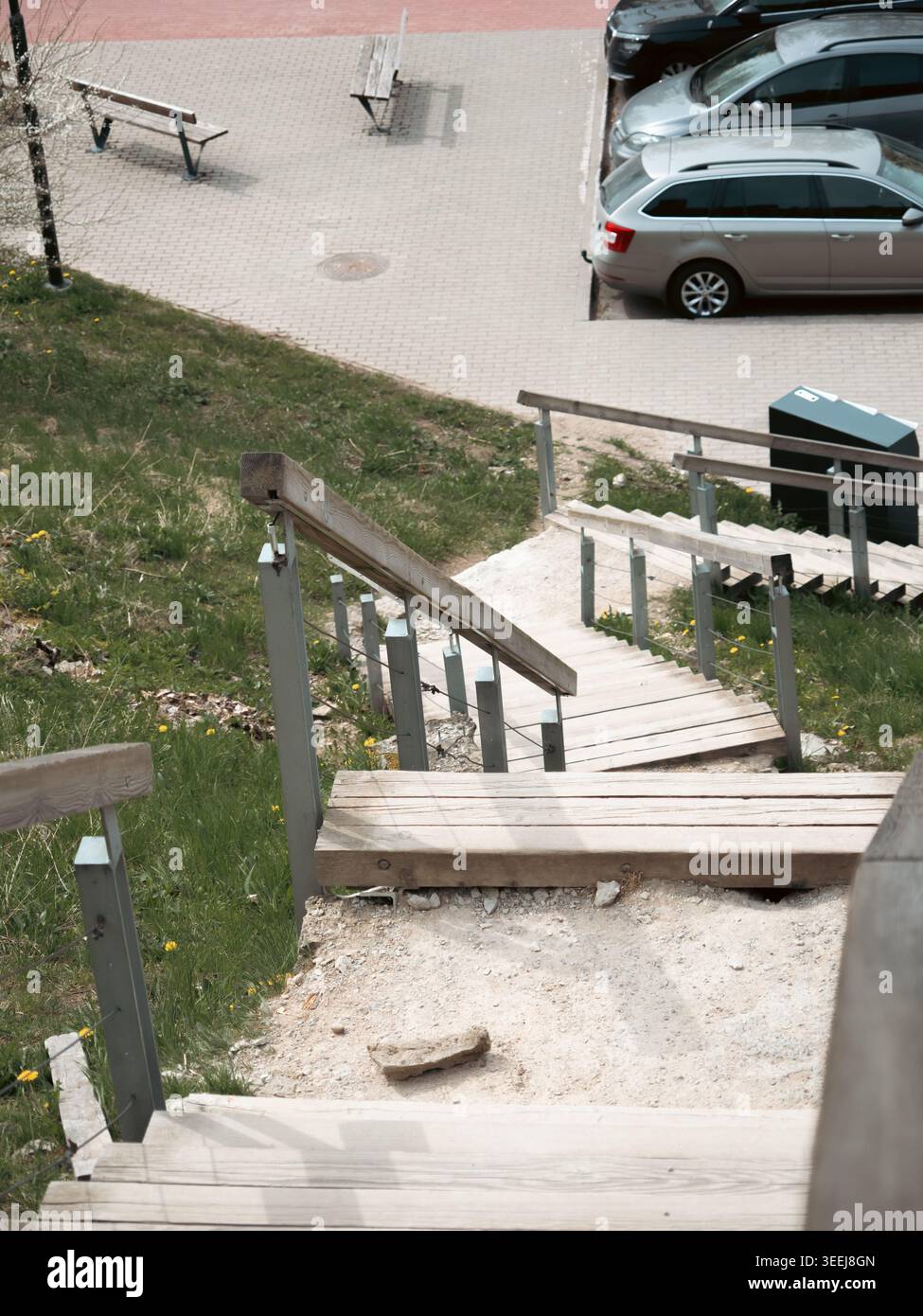 Holztreppe mit Metallgeländer, die einen grasbewachsenen Hügel hinabführt zu einem gepflasterten Parkplatz in Rakvere, Estland Stockfoto