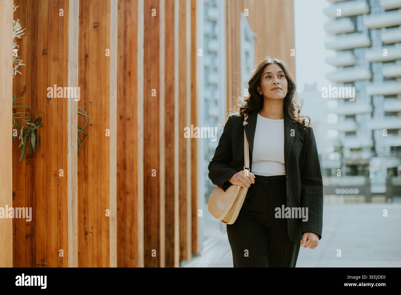 Eine stilvolle Frau schlendert souverän durch markante Holzgebäude und genießt die lebhafte urbane Atmosphäre und den hellen Sonnenschein. Stockfoto
