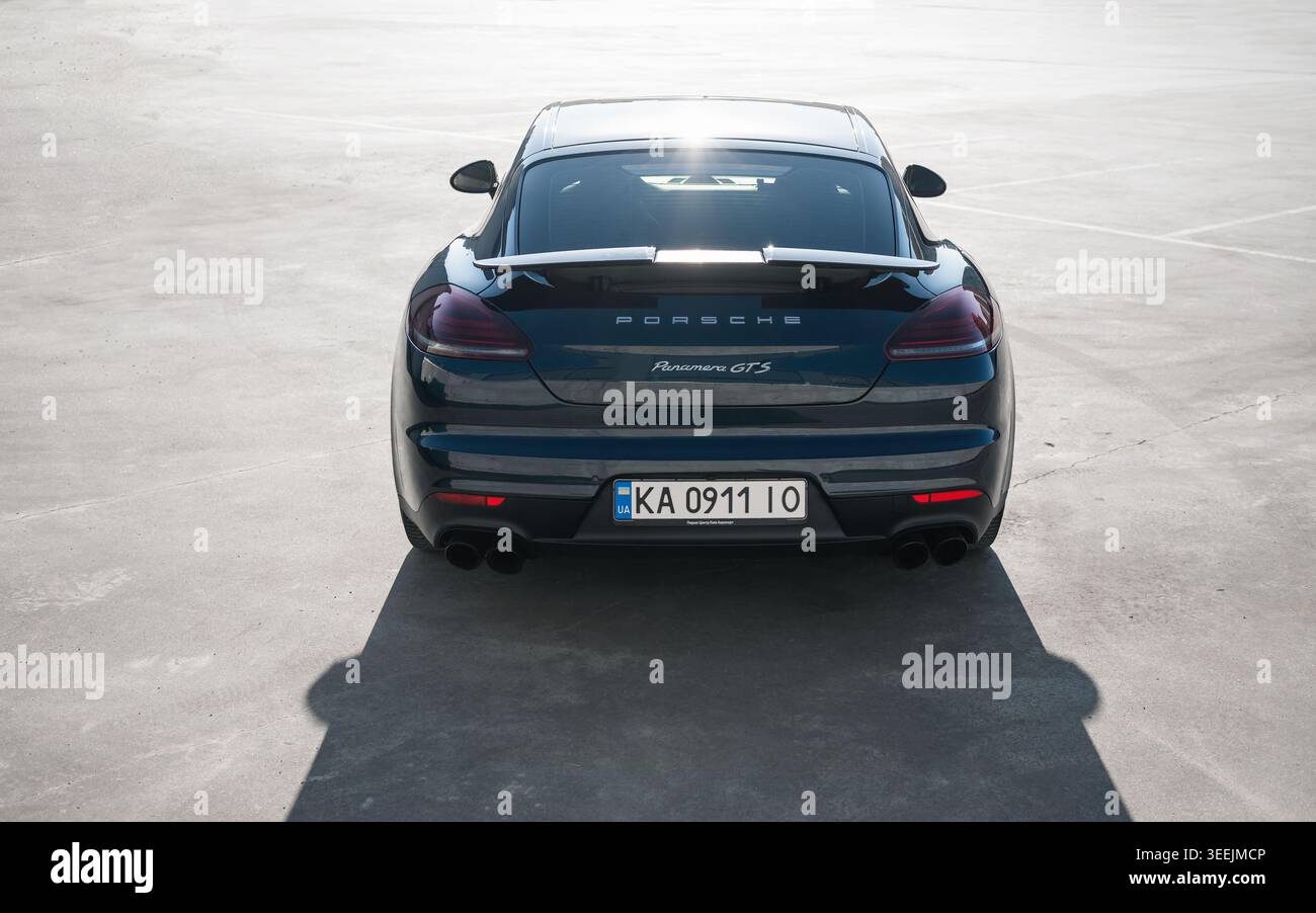 Dunkelblauer Porsche Panamera auf einem großen Parkplatz. Rückansicht des deutschen Grand Tourers, der auf einer riesigen Betonoberfläche geparkt ist, von hinten strahlende Sonne. Stockfoto