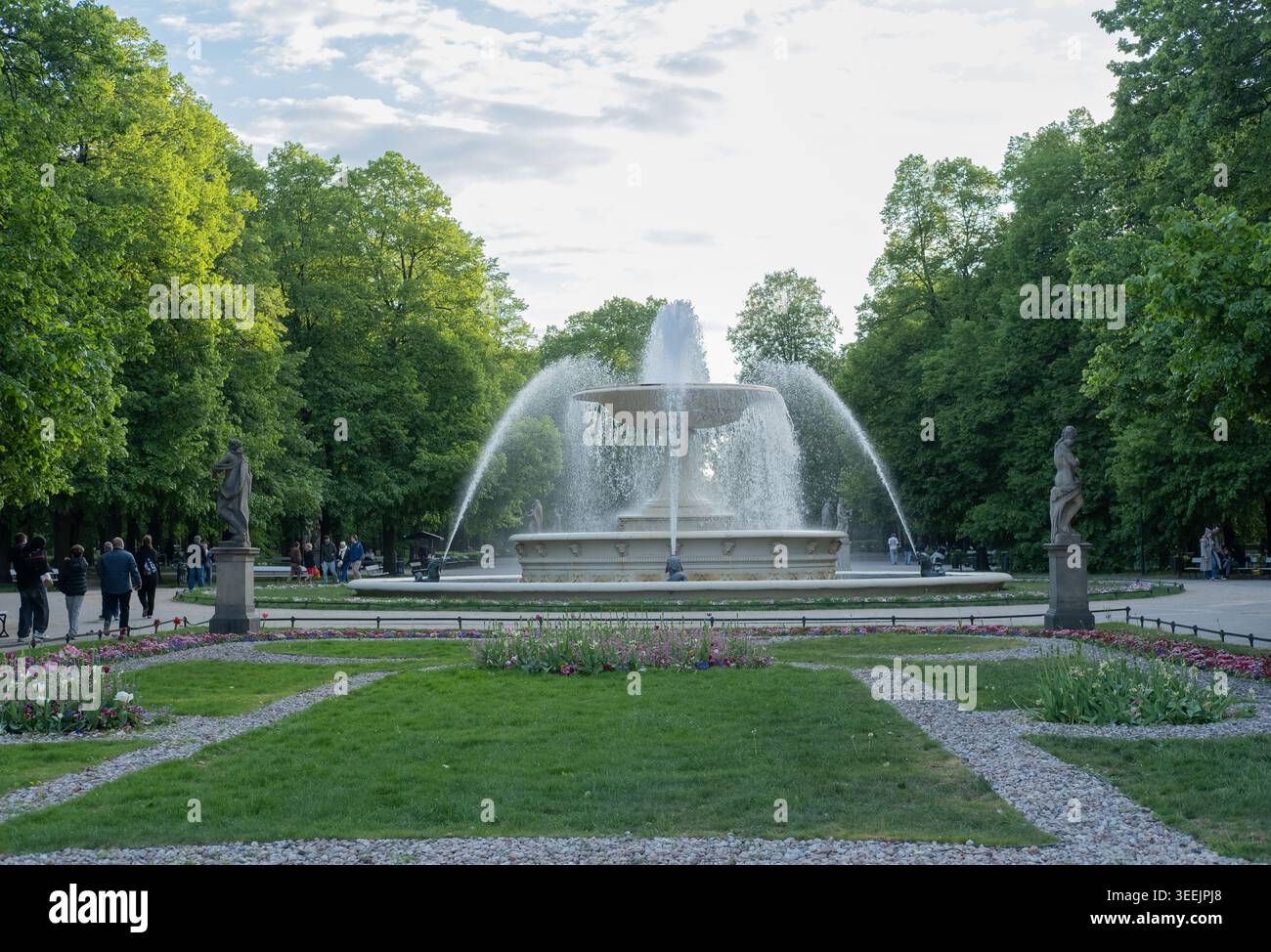 Großer Steinbrunnen, der Wasser im Zentrum eines üppig grünen Stadtparks sprüht. Stockfoto