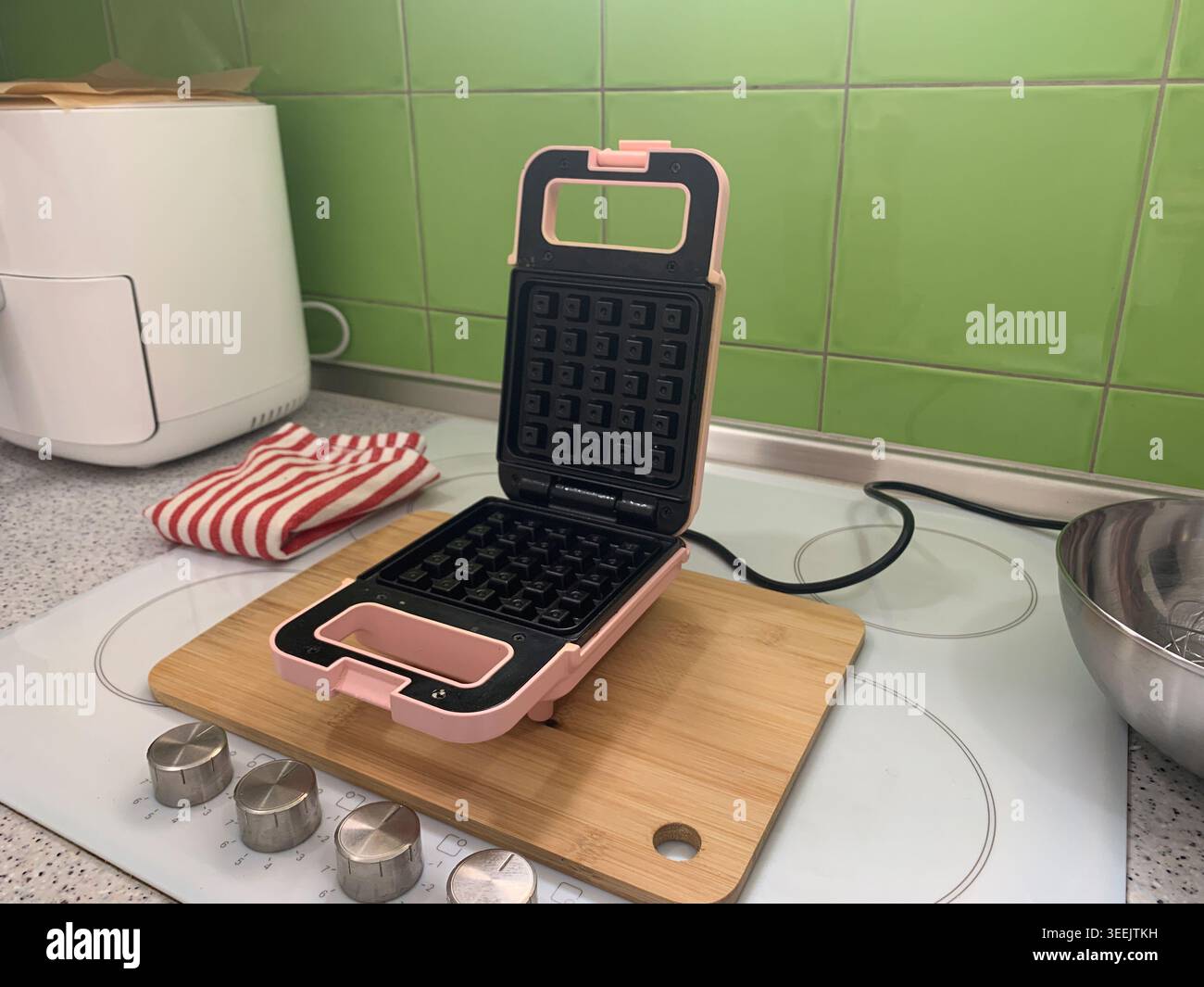Hoher rechtwinkliger Blick auf eine offene pinkfarbene Waffelmaschine und ein weißes Gerät auf einer Küchenzeile. Stockfoto