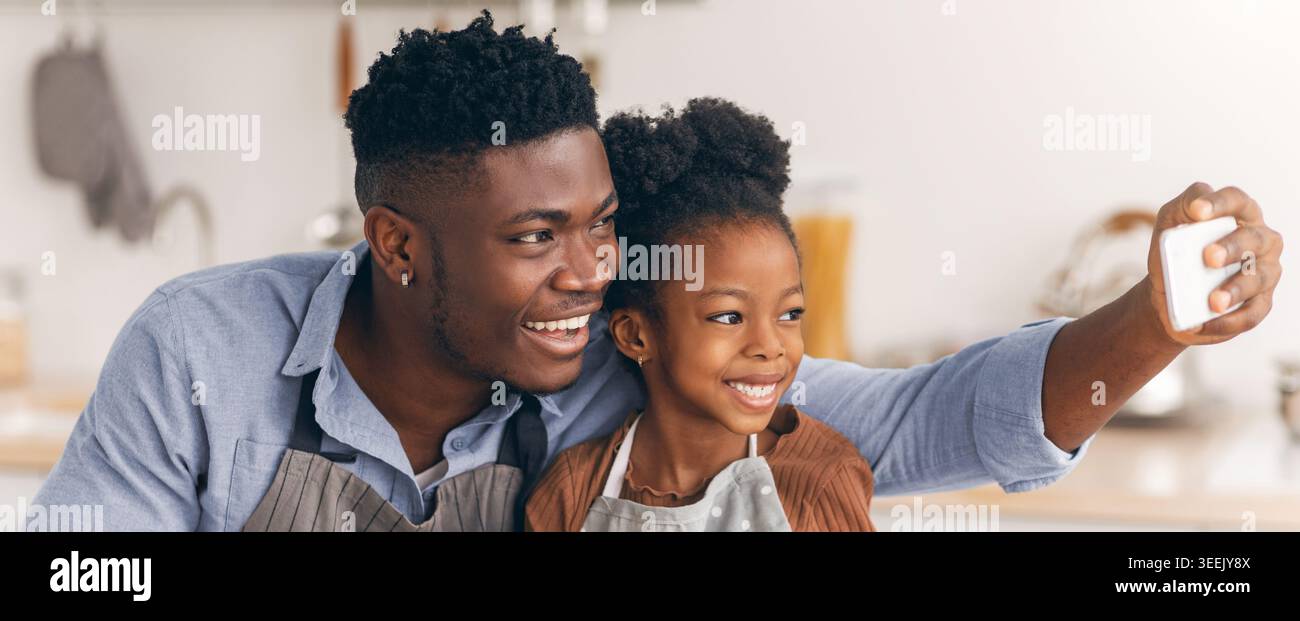 Vater und Tochter teilen sich einen Moment, während sie ein Selfie in einer hellen Küche machen Stockfoto