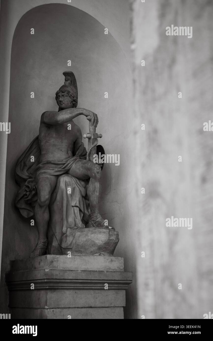 Klassische Kriegerstatue mit Schwert und Helm in bogenförmiger Nische, Schwarzweiß-Kunstfotografie Stockfoto