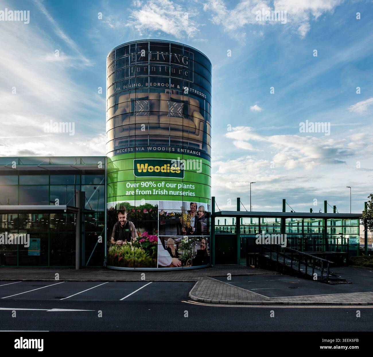 Woodie's und EZ Living Furniture Einzelhandel in Dublin, Irland. Zylindrischer Glasturm mit großen Anzeigen unter blauem Himmel mit Wolken. Stockfoto