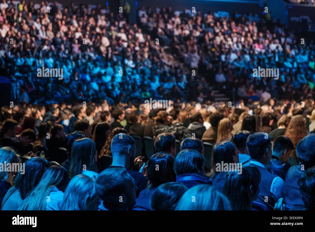Voller Zuschauer, der die Keynote bei einer Konferenz in der Halle ansieht, blaue Bühnenbeleuchtung, konzentriertes Publikum, Networking-Atmosphäre. Stockfoto