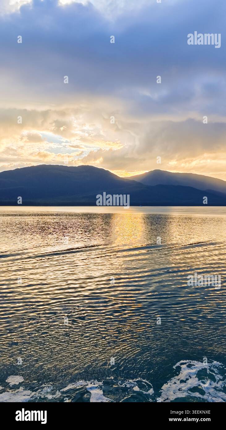 Alaska, USA - 13. August 2024: Blick auf die Chatham Strait mit einer Silhouette der Bergkette bei Sonnenuntergang, mit Wasserkräuseln und bewölktem Himmel in A Stockfoto