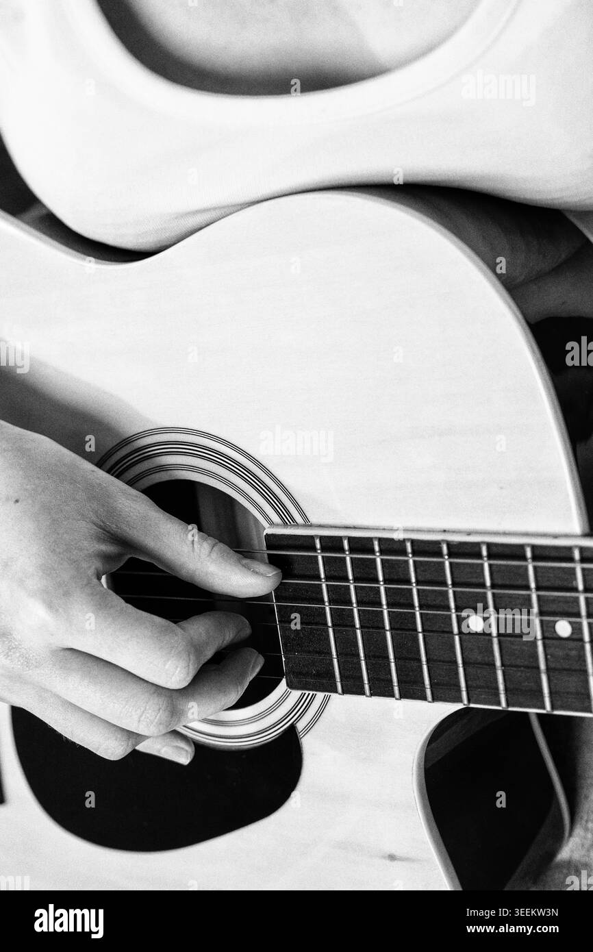 Frau spielt Akustikgitarre. Nahaufnahme der Hand an Strings. Hobby- und kreative Freizeitaktivitäten. Einfarbige künstlerische Aufnahme mit Filmmarnung und selektiv Stockfoto