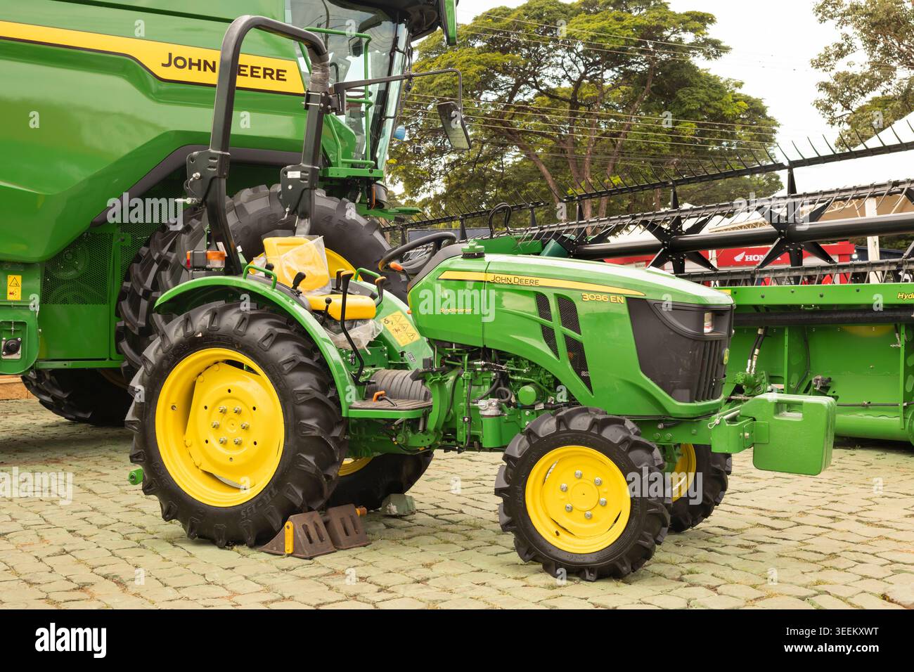 Kompakttraktor John Deere 3036EN, der neben einem landwirtschaftlichen Erntemaschine mit knickgelenktem Schneidwerk geparkt ist. Stockfoto