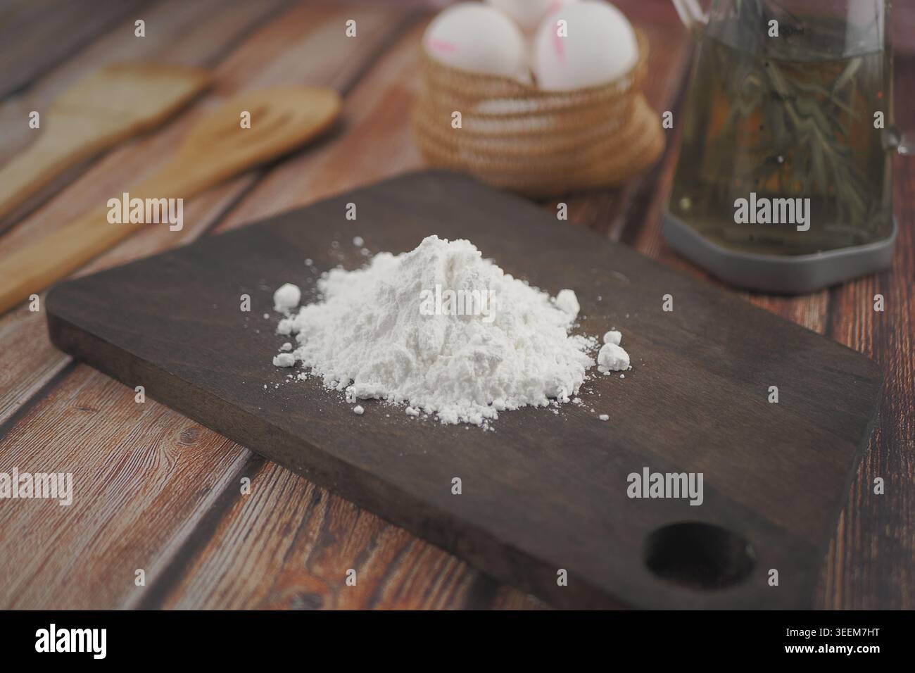 Mehl auf einem Holzbrett mit Eiern und Öl im Hintergrund Stockfoto