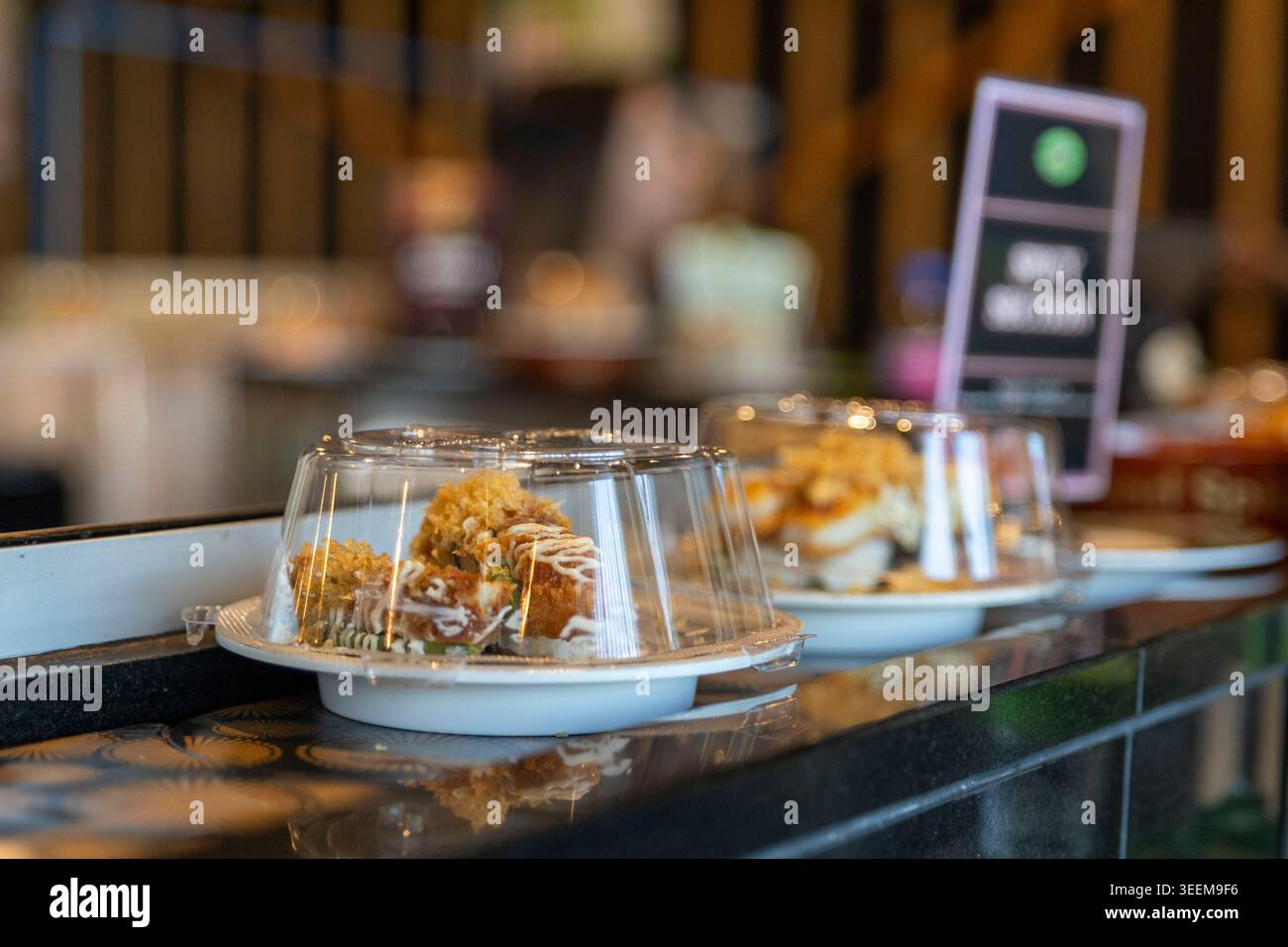 Nahaufnahme einer Sushi-Rolle unter einer Plastikabdeckung auf einem beweglichen Förderband in einem japanischen Sushi-Zug-Restaurant in Brisbane. (2025) Stockfoto