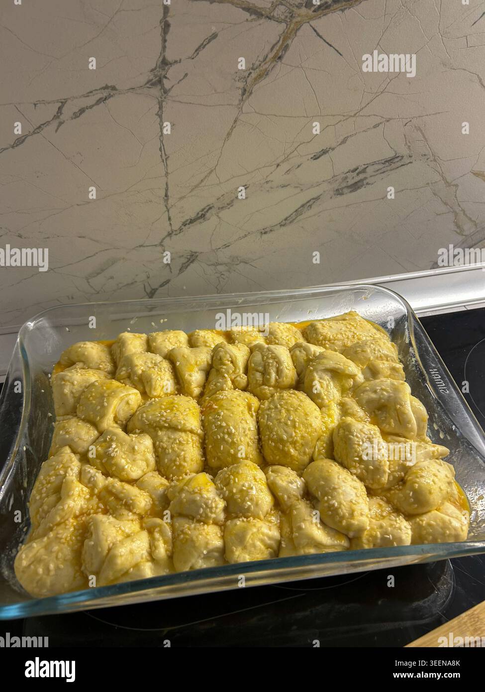 Hausgemachte Teigbrötchen mit Sesamsamen in einer Glasbackform, bereit zum Backen im Home-Backen. - Smartphone-aufgenommenes Stockfoto