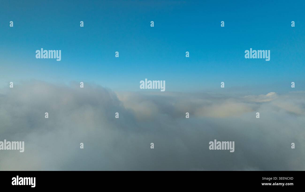 Ein atemberaubender Blick auf den Sonnenaufgang über einem riesigen Wolkenmeer mit fernen Bergsilhouetten unter einem klaren blauen Himmel. Perfekt für Themen der Ruhe, na Stockfoto