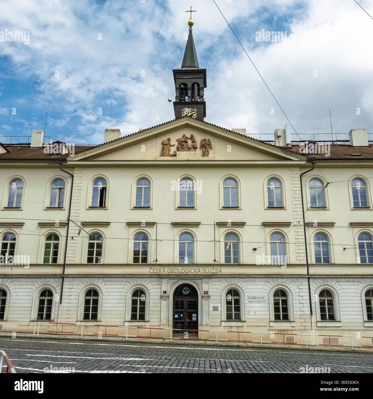 Fassade Des Eleganten Tschechischen Geologischen Vermessungsgebäudes Mit Kirchturm Und Kruzifix Gegen Den Bewölkten Himmel, Prag, Tschechische Republik. Stockfoto