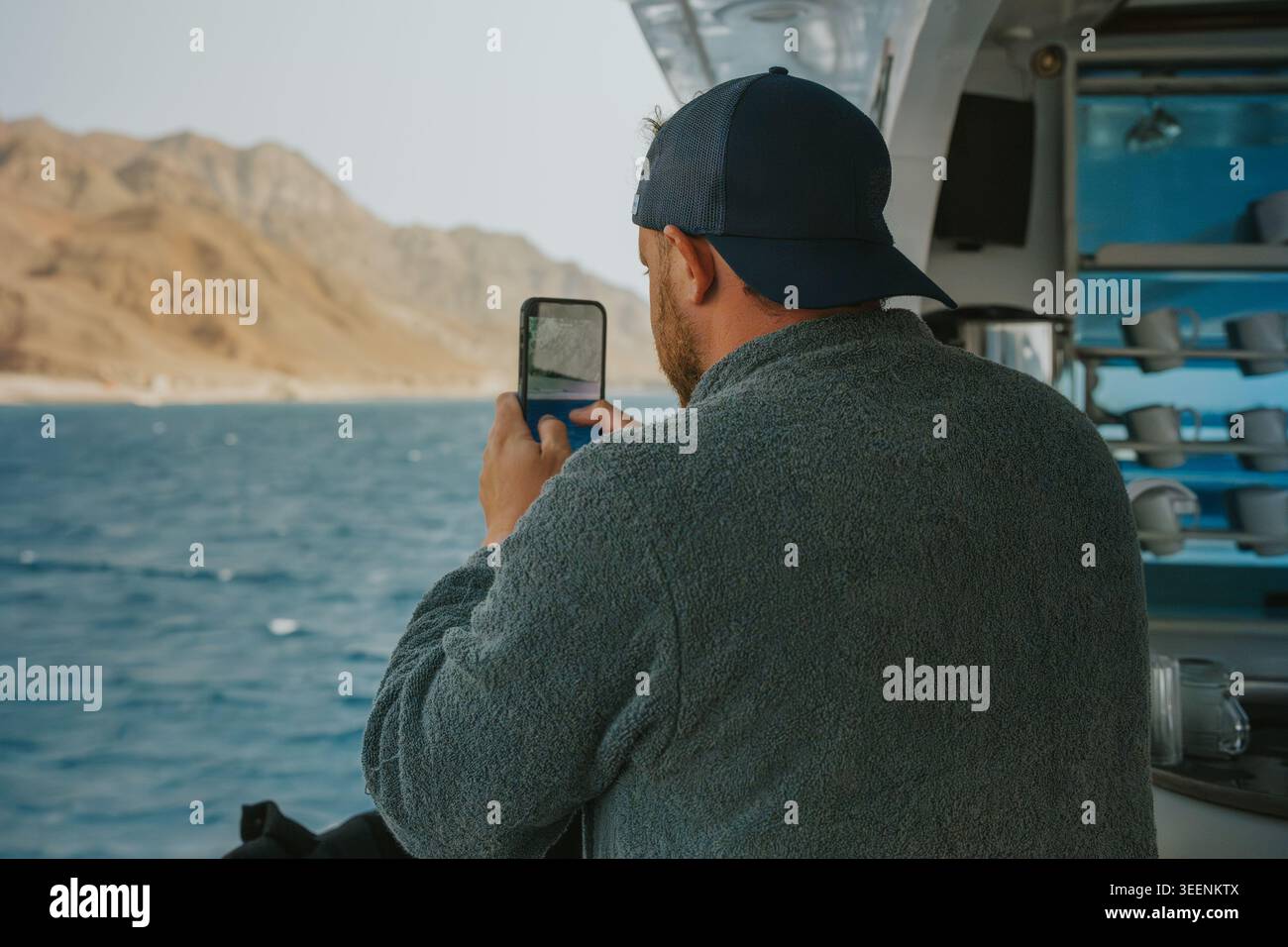 Mann auf einem Boot nimmt mit seinem Smartphone eine Küstenlandschaft auf Stockfoto