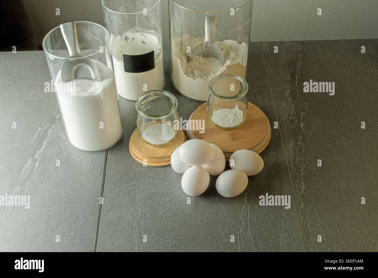 Einfache Zutaten für einen hausgemachten Biskuitteig auf einer dunklen Küchentheke, die eine authentische und zugängliche tägliche Backzubereitung zeigt Stockfoto