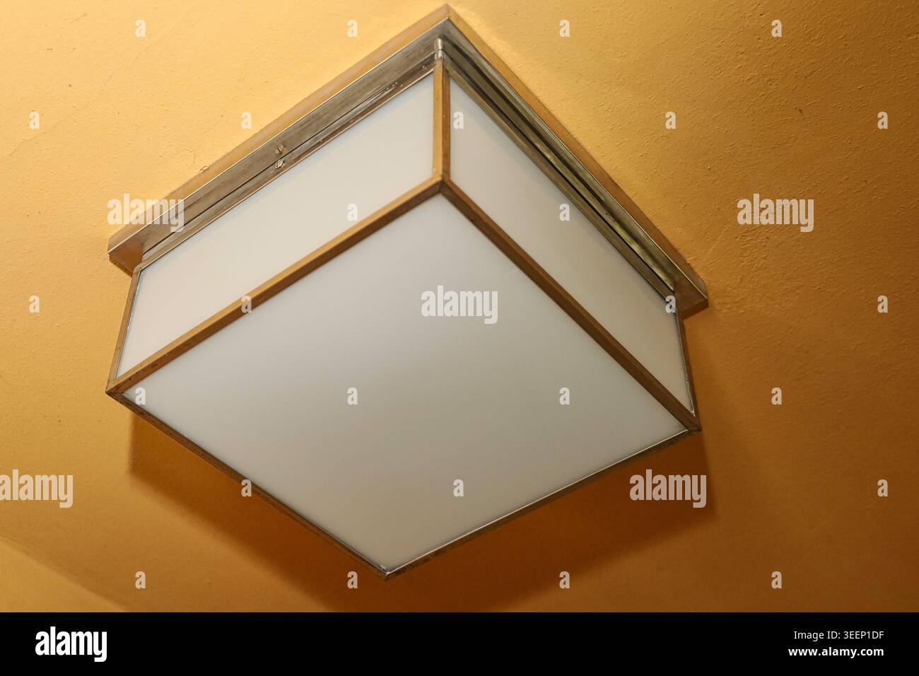 Bauhaus-Design im Haus Rabe in Zwenkau: Quadratische Deckenleuchte aus mattiertem Glas und Metall an einer ockerfarbenen Decke Stockfoto