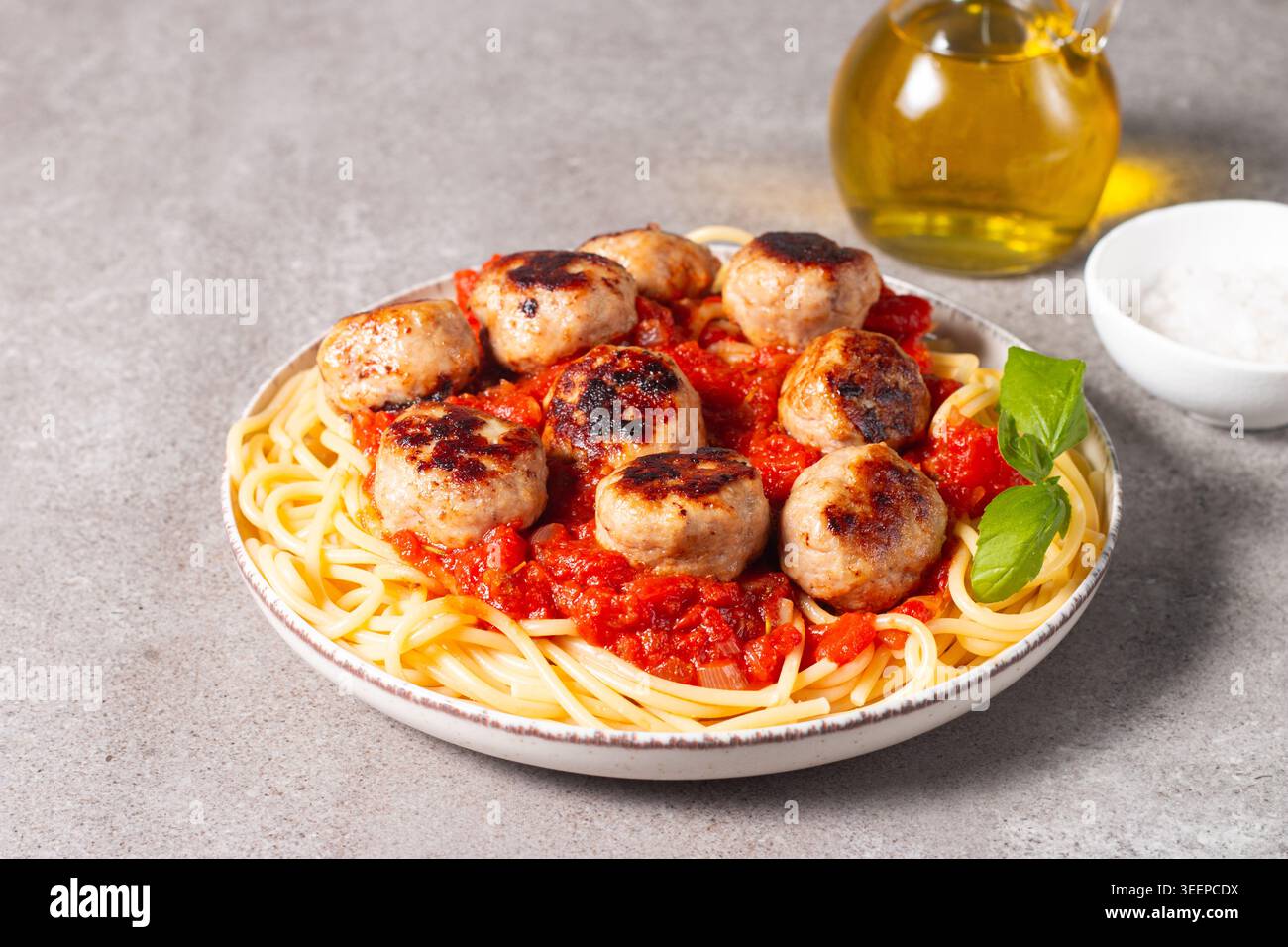 Ein Teller mit klassischen Spaghetti, garniert mit gebräunten Fleischbällchen und reichhaltiger Tomatensauce auf einem leichten Keramikgericht. Stockfoto