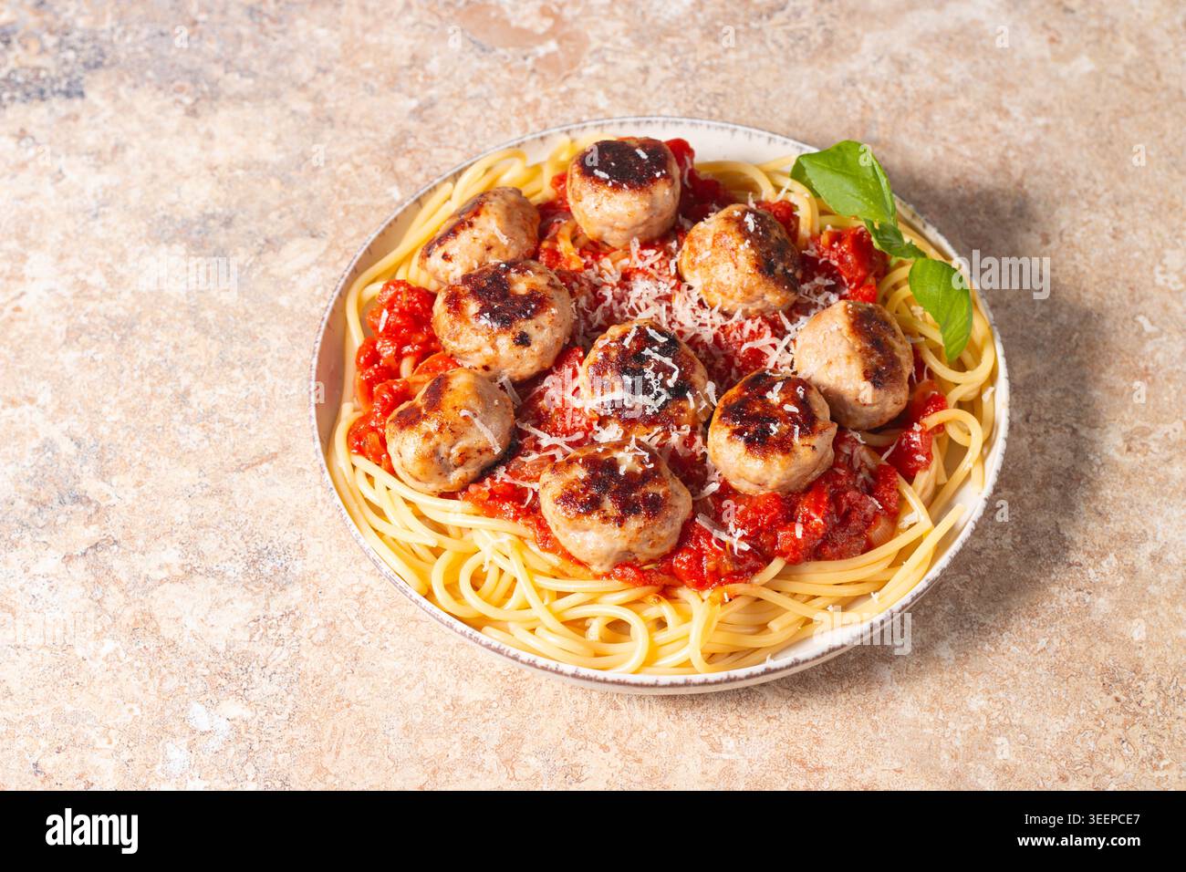 Ein Teller mit klassischen Spaghetti, garniert mit gebräunten Fleischbällchen und reichhaltiger Tomatensauce auf einem leichten Keramikgericht. Stockfoto