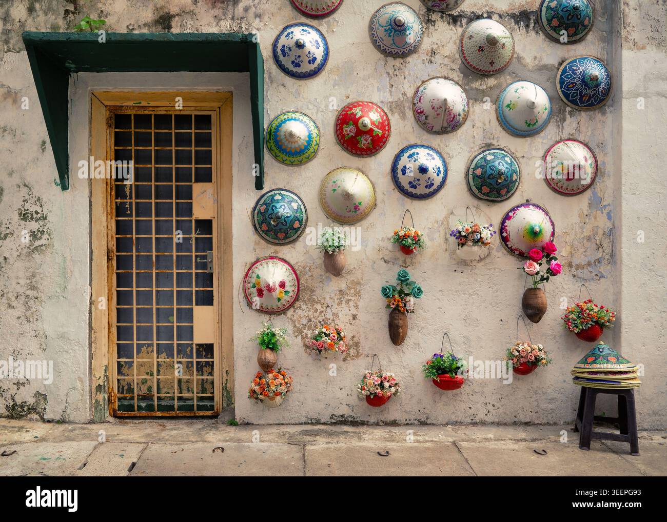 Farbenfrohe konische Hüte auf einer rustikalen, verwitterten Wand in den Seitenstraßen von Ipoh, Malaysia, schaffen eine lebendige Mischung aus Tradition und Charme. Stockfoto