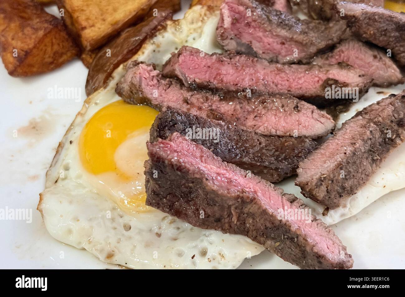 Mittelgroßes, in Scheiben geschnittenes Steak mit gerösteten Kartoffelscheiben und Spiegelei in rustikalem Gourmetstil. Stockfoto