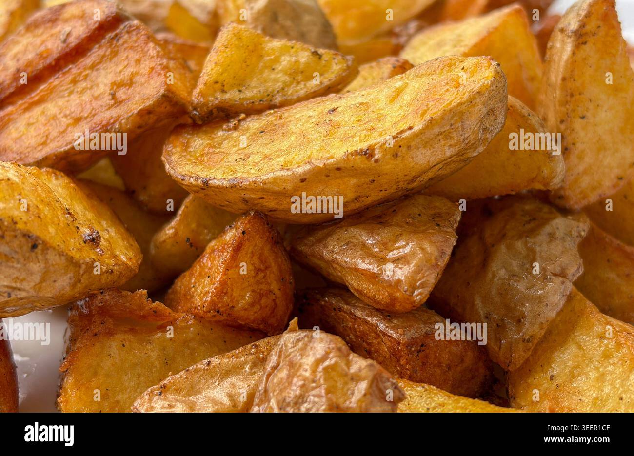 Nahaufnahme von knusprigen gebratenen Kartoffelscheiben mit goldbraunen Gewürzen und rustikaler, gekochter Textur. Stockfoto